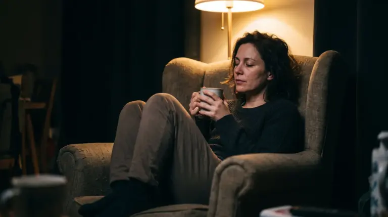 Žena uveče sedi u fotelji sa šoljom u ruci